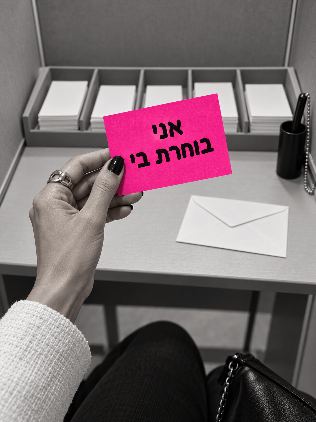 יד מחזיקה פתק ורוד עם הכיתוב אני בוחרת בי בתוך תא הצבעה
